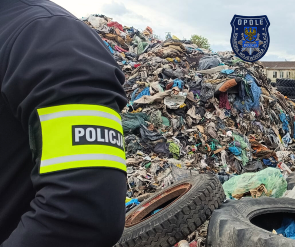 Zdjęcie przedstawia wysypisko śmieci, na pierwszym planie funkcjonariusz.